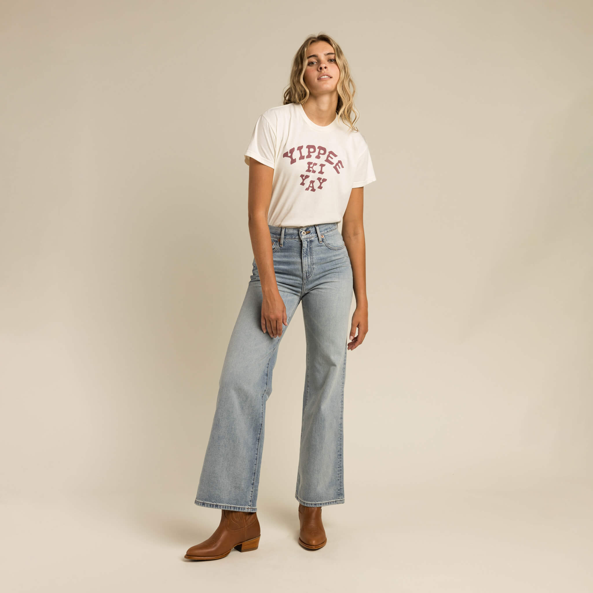 Woman wearing a white t-shirt with text and blue jeans on a beige background